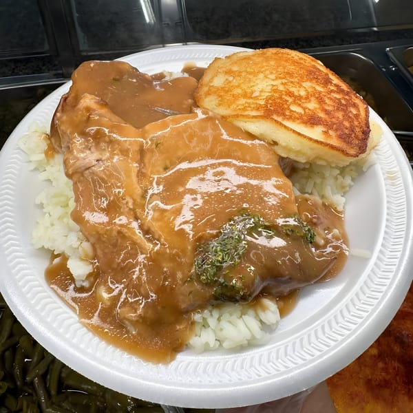Southern-style pork chop with gravy, rice, and a golden-brown cornbread on a white plate.