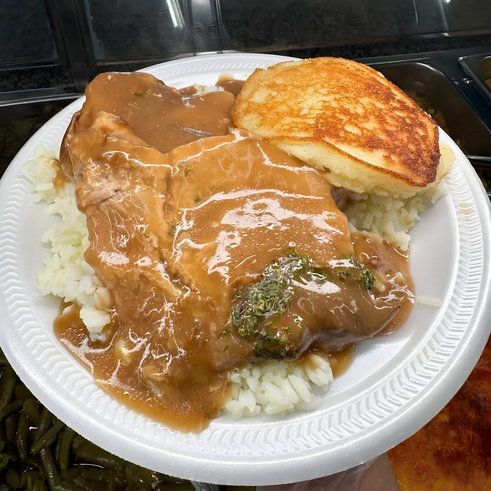 Southern-style pork chop with gravy, rice, and a golden-brown cornbread on a white plate.