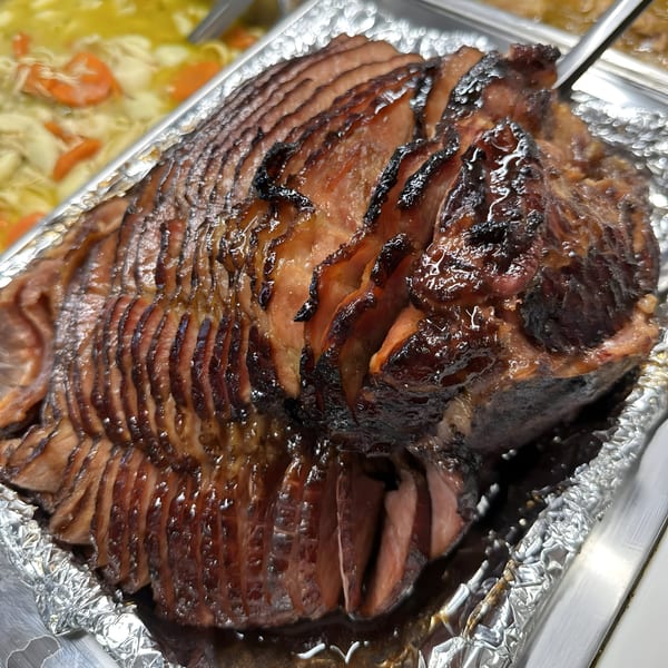 A large, glazed, spiral-sliced ham in a foil-lined serving pan at Ramzys Meat & Three.